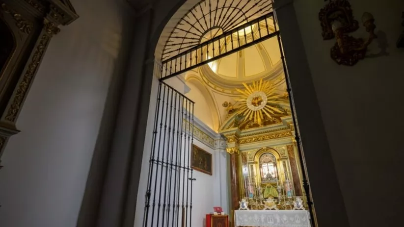 Capilla lateral vista tras una reja alta, con altar y decoración dorada.