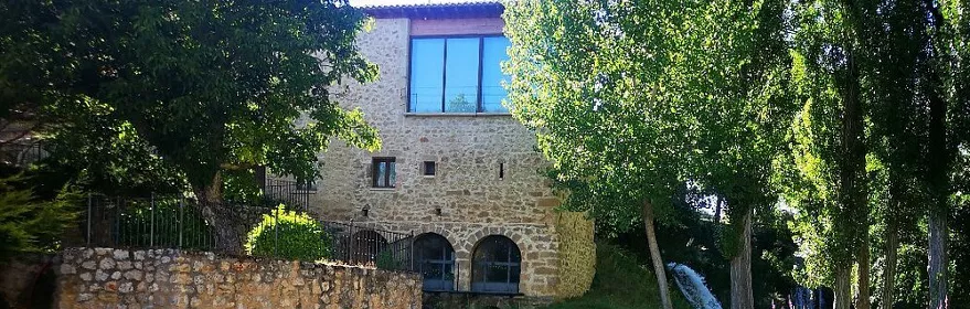 Casa de piedra junto a río y vegetación.