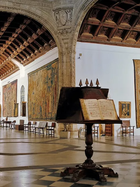 Sala histórica con artesonado de madera y tapices colgados en las paredes.