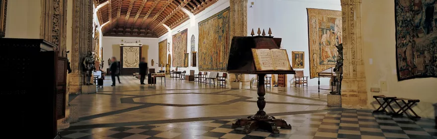 Sala histórica con artesonado de madera y tapices colgados en las paredes.