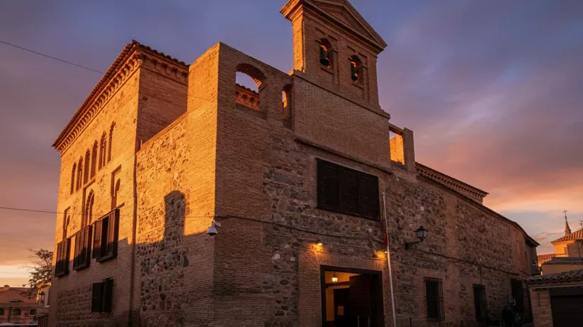 Fachada histórica de ladrillo y piedra iluminada al atardecer.