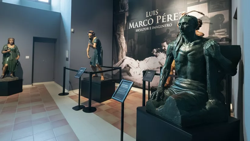 Esculturas religiosas en sala oscura con panel informativo.