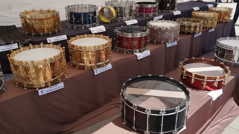 Exposición de tambores decorados sobre mesas con etiquetas informativas.