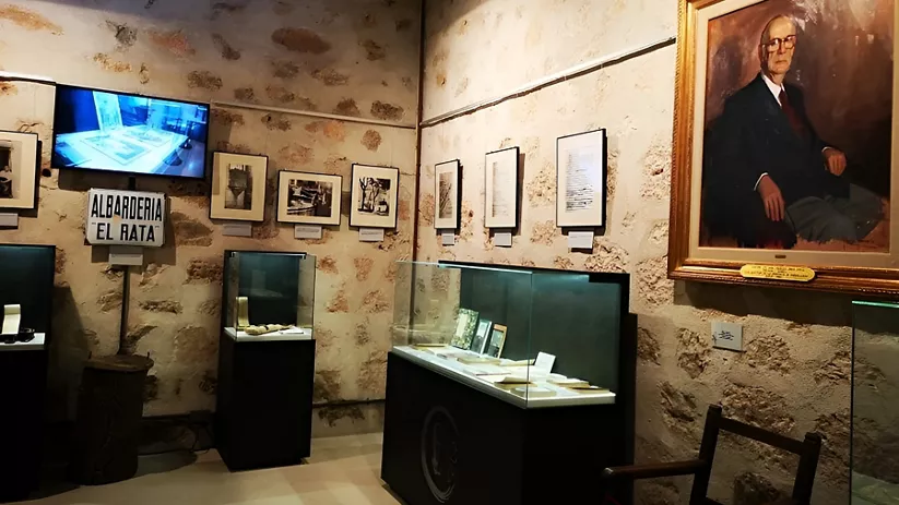 Sala de museo con vitrinas y retrato.