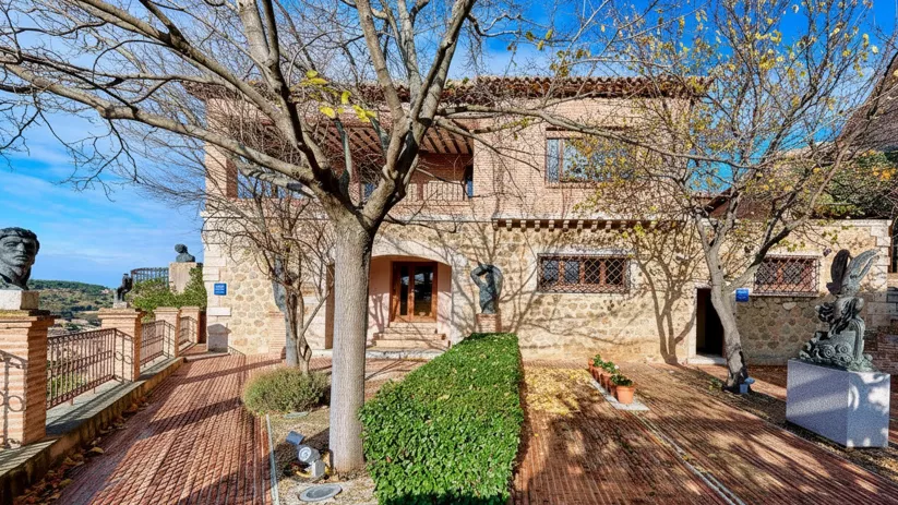 Jardín con senderos de ladrillo, esculturas y vivienda tradicional.