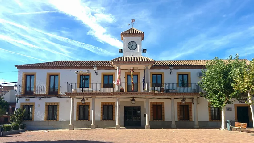 Fachada de edificio municipal blanco con reloj, soportales y banderas