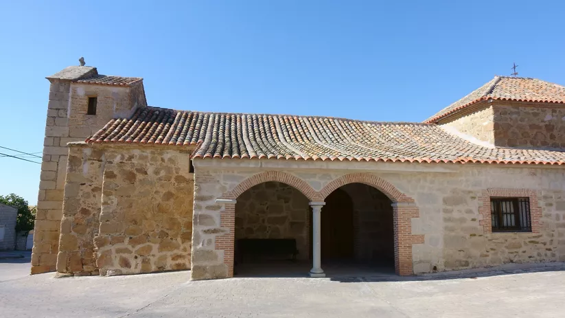 Iglesia de piedra con pórtico de arcos y tejado de teja
