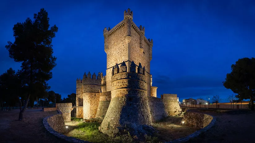 Torre defensiva iluminada de noche con murallas de piedra