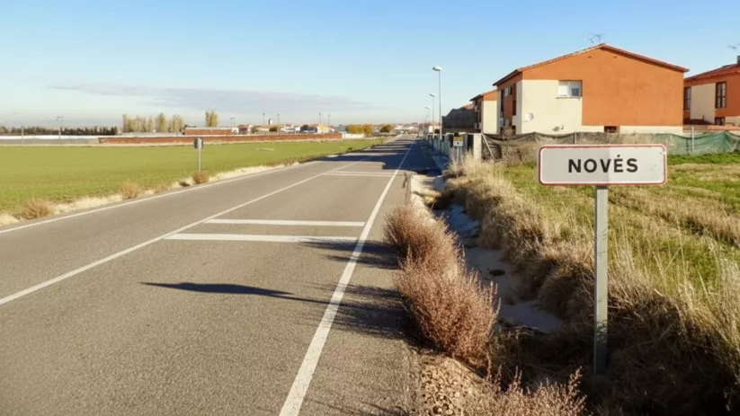 Carretera de entrada al pueblo junto a campos y viviendas
