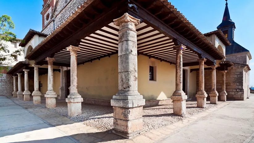 Pórtico de piedra con columnas y cubierta de madera visto en perspectiva.