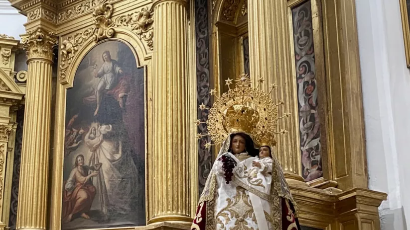 Escultura coronada junto a retablo dorado.