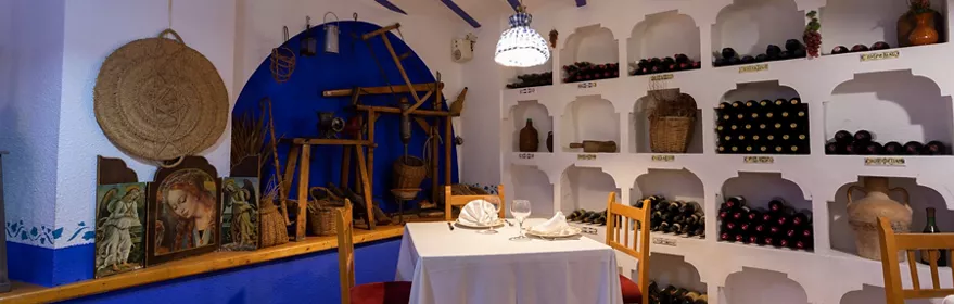 Comedor tradicional con mesa vestida y botellas en nichos de pared