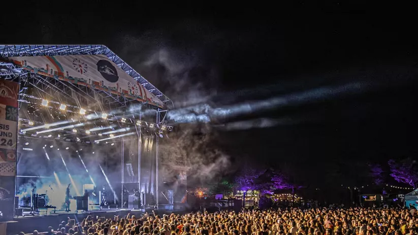 Escenario iluminado de noche con público asistiendo a concierto