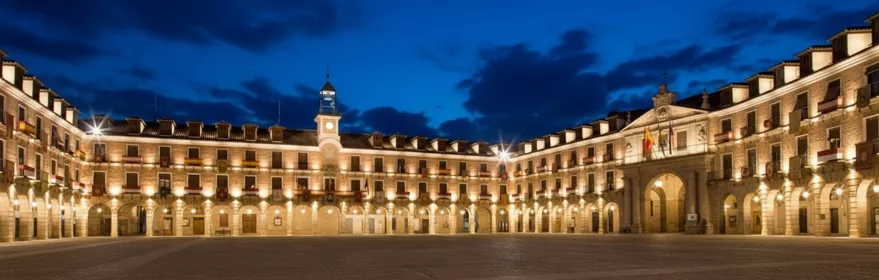 Plaza monumental iluminada de noche con arcos y reloj