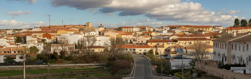 Carretera de entrada al pueblo con casas y cielo nuboso