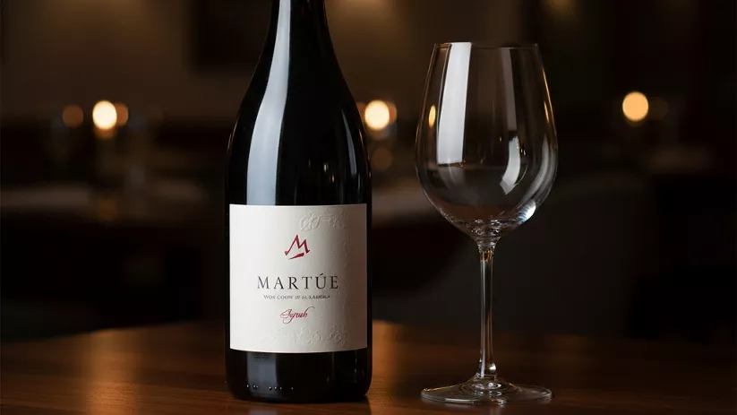 Botella de vino tinto y copa vacía en una mesa de restaurante con ambiente tenue.