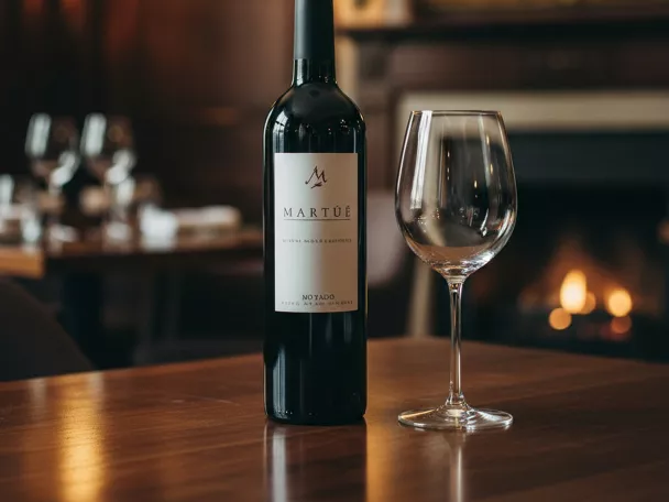 Botella de vino tinto y copa vacía en primer plano sobre mesa de restaurante.