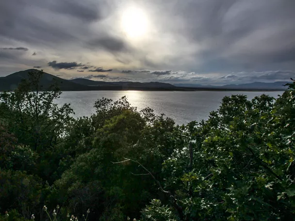 Embalse rodeado de árboles con montañas bajo cielo nublado.