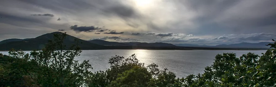 Embalse rodeado de árboles con montañas bajo cielo nublado.