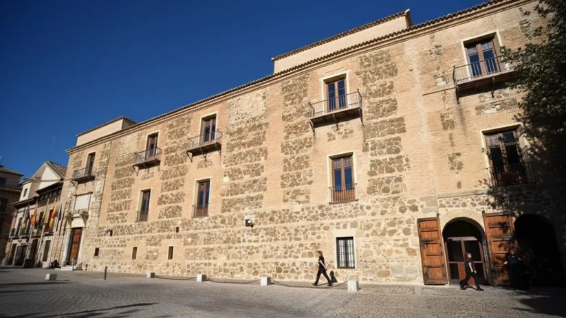 Vista lateral de palacio de piedra con balcones y puerta abierta.