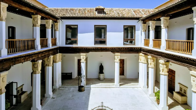 Patio interior con columnas blancas, galerías de madera y pozo central.