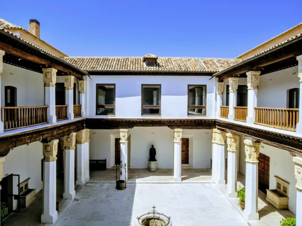 Patio interior con columnas blancas, galerías de madera y pozo central.