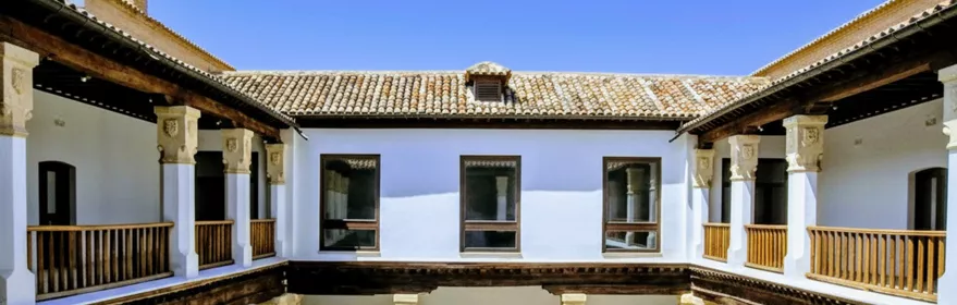 Patio interior con columnas blancas, galerías de madera y pozo central.