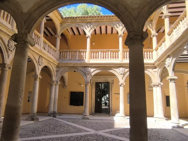 Patio interior con arcos de piedra, columnas y suelo empedrado iluminado por luz natural.