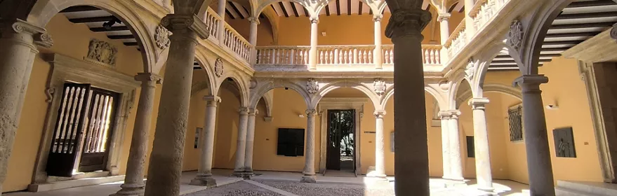 Patio interior con arcos de piedra, columnas y suelo empedrado iluminado por luz natural.