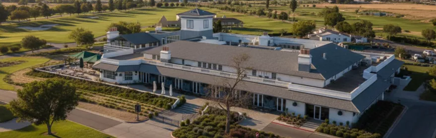 Vista aérea de un club junto a un campo de golf, con montañas al fondo.