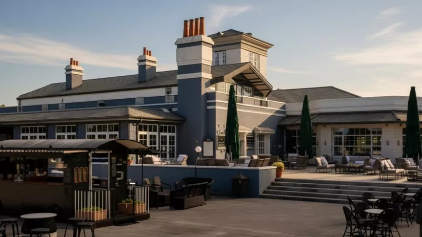 Terraza exterior con mesas y sombrillas frente a un edificio de estilo club.