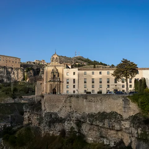 Edificio monumental sobre muralla con colina al fondo.