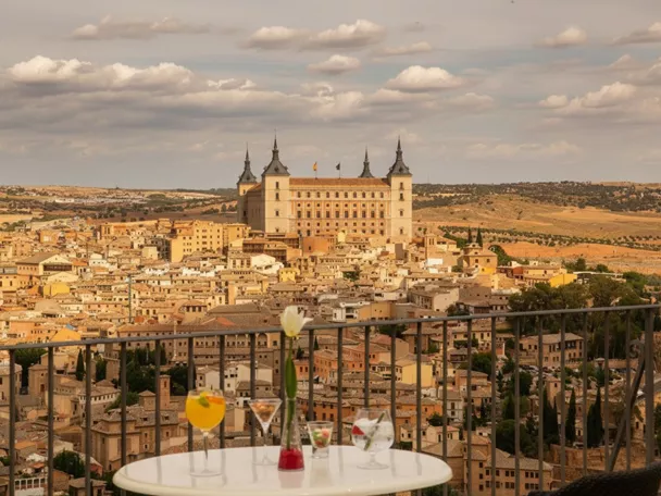 Terraza con copas frente a panorámica urbana dominada por gran edificio monumental.