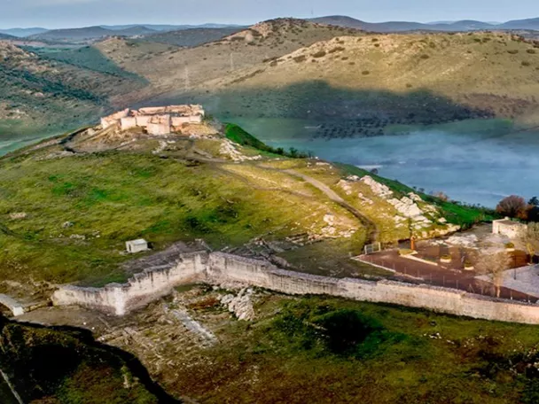 Vista aérea de recinto amurallado sobre colina con niebla en el valle