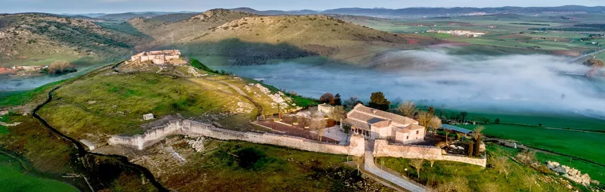 Vista aérea de recinto amurallado sobre colina con niebla en el valle