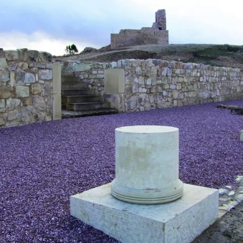 Parte de columna del yacimiento arqueológico con castillo atrás