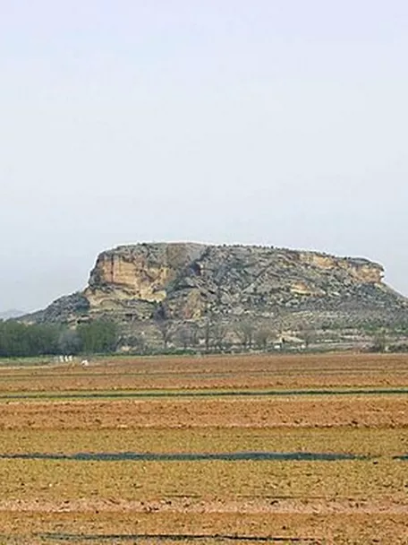 Meseta rocosa aislada vista desde campos agrícolas en primer plano.