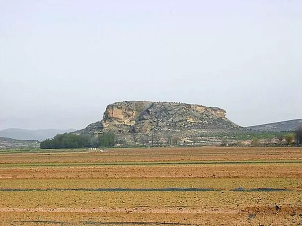 Meseta rocosa aislada vista desde campos agrícolas en primer plano.