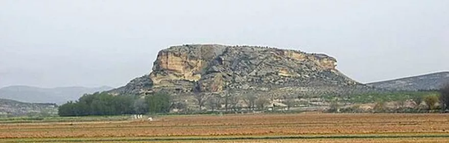 Meseta rocosa aislada vista desde campos agrícolas en primer plano.