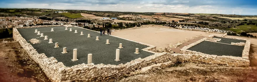 Ruinas arqueológicas con columnas bajas y muros de piedra en una colina.