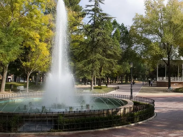 Fuente circular con surtidor alto en parque arbolado.