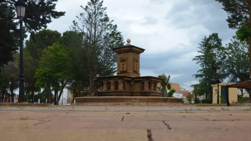 Fuente de piedra en una plaza arbolada.