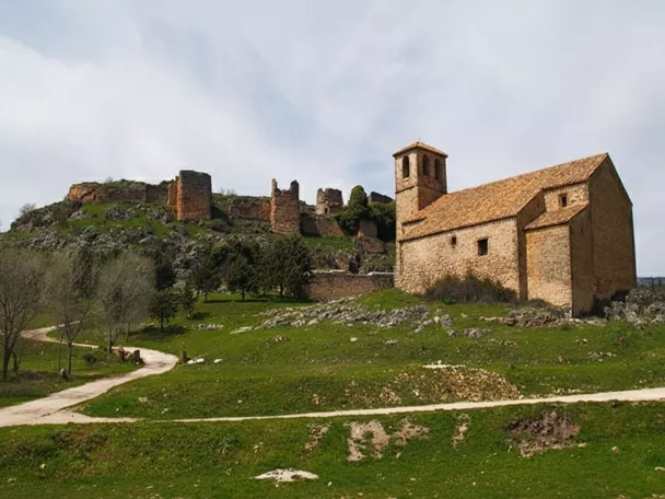Iglesia de piedra en una colina verde, con ruinas de un castillo al fondo.