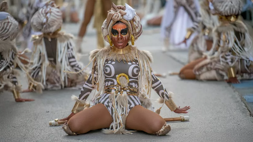 Bailarina caracterizada con maquillaje tribal y vestuario étnico durante un desfile.