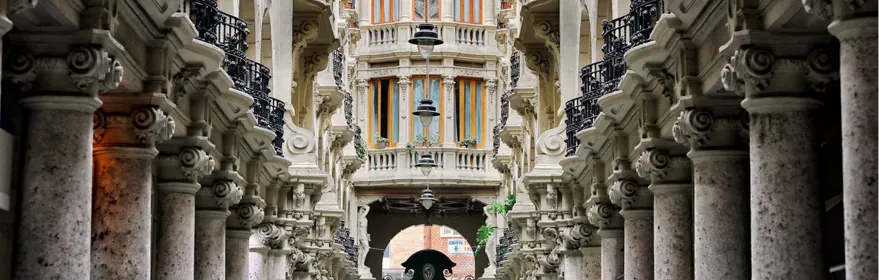 Galería interior simétrica con columnas de piedra, balcones de hierro y techo acristalado.
