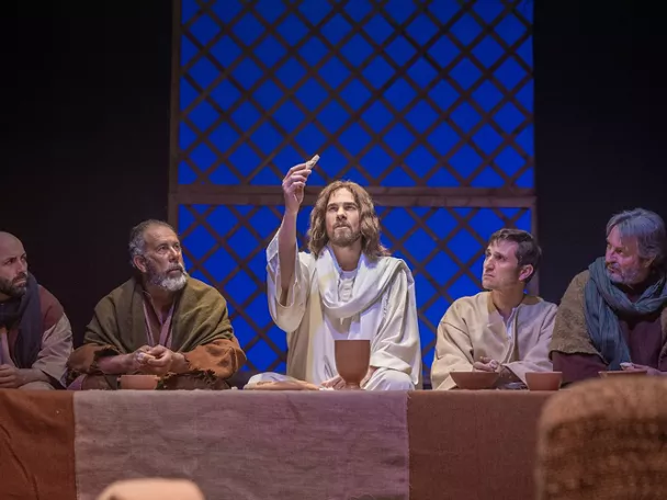 Grupo de hombres comparte pan y vino en una cena teatral