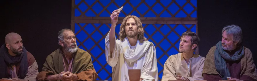 Grupo de hombres comparte pan y vino en una cena teatral