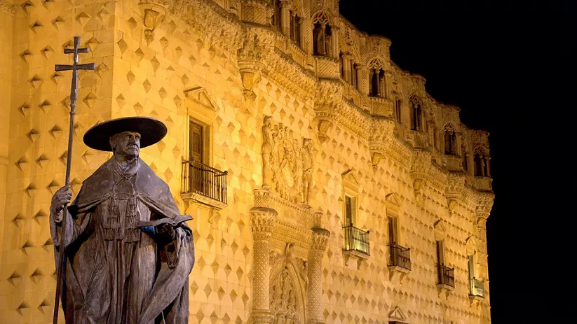 Estatua histórica frente a palacio monumental iluminado.