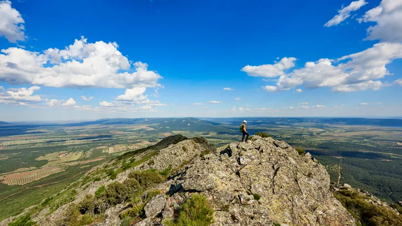 Persona en la cima de una montaña con paisaje abierto al fondo.