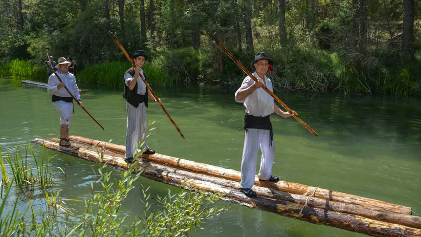 Hombres guiando troncos flotantes con varas.